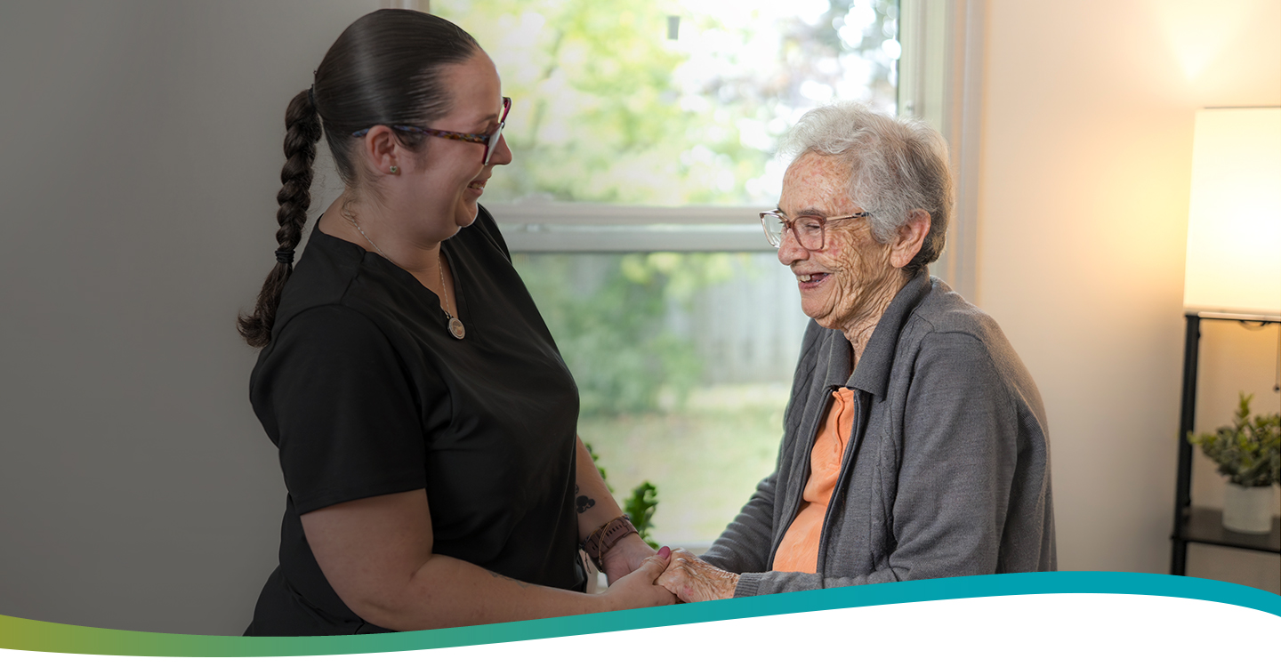 Smiling caregiver supporting an elderly resident in her suite at Atrium Retirement Residence in Orillia.